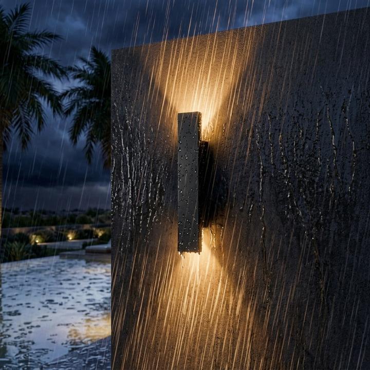 Black wall light on a dark textured wall in heavy rain with water droplets on its surface.