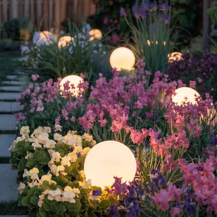 Glowing orb lights among pink, purple and cream flowers along a garden walkway