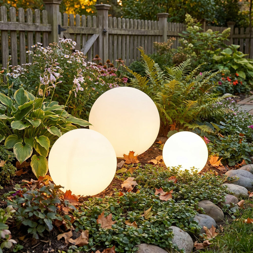 Three white orb lights among hostas and ferns beside a wooden picket fence