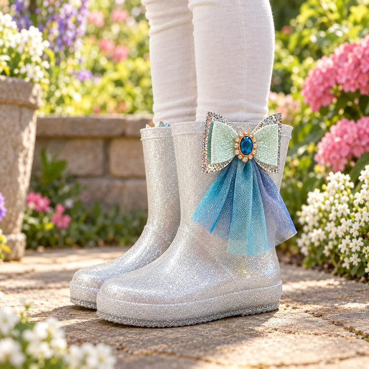 Child wearing silver glitter rain boots outdoors, each with a mint glitter bow, blue gem and flowing blue tulle. 1