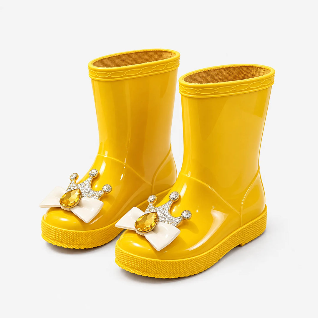 Pair of glossy yellow rain boots angled from the front, each topped with a cream bow, gold crown and yellow gem. 5