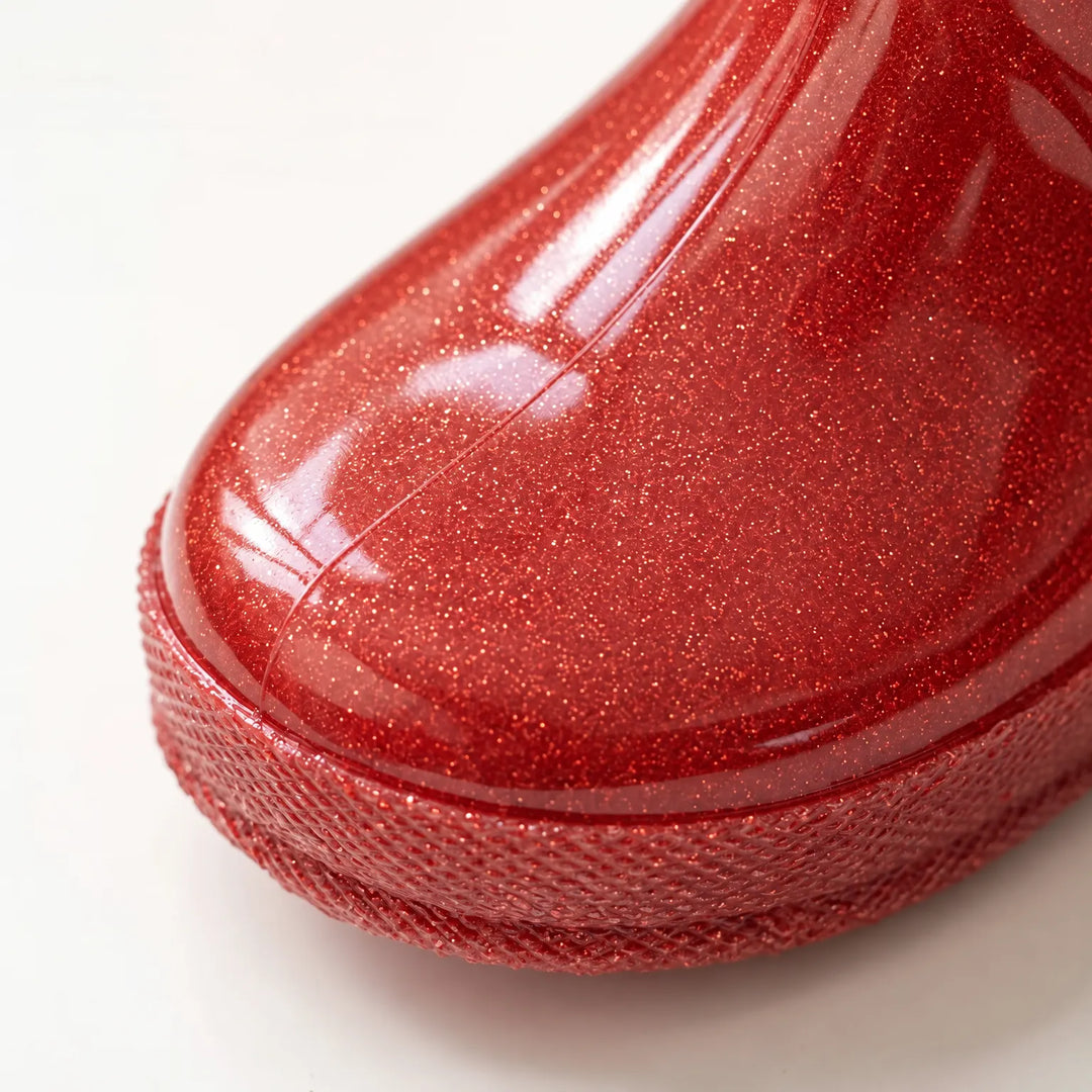 Close-up of the toe of a red glitter rain boot showing the sparkly finish and textured sole edge. 6