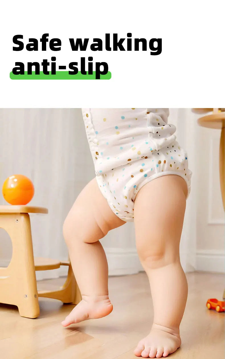 Baby in a polka-dot bodysuit standing on a wood floor near a wooden stool and orange ball 15