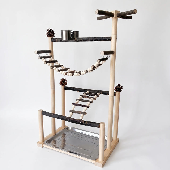 Angled view of a tall wooden bird play stand with natural branch perches, bead-and-twig ladders, pine cones, a steel cup and a steel tray. 1