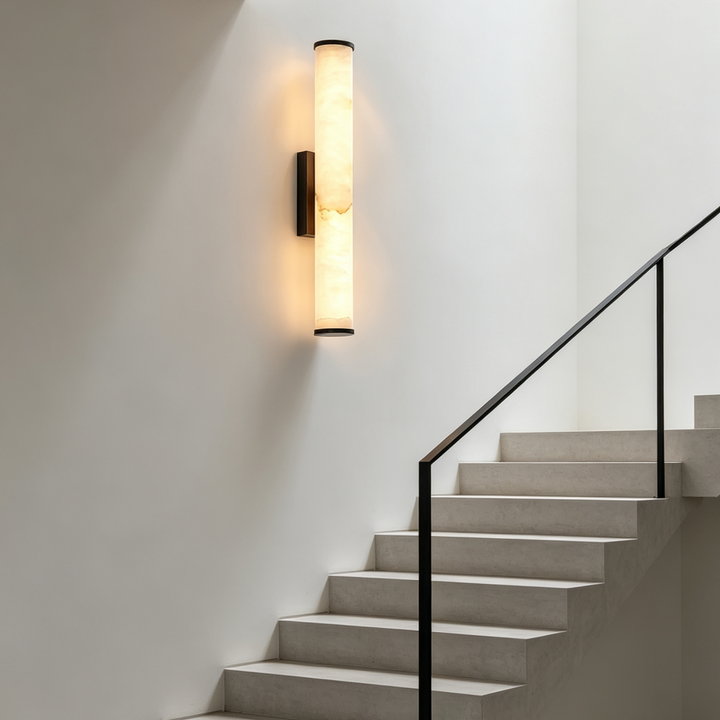 Illuminated marble sconce on a white stairwell wall beside a concrete staircase with a slim black metal handrail.