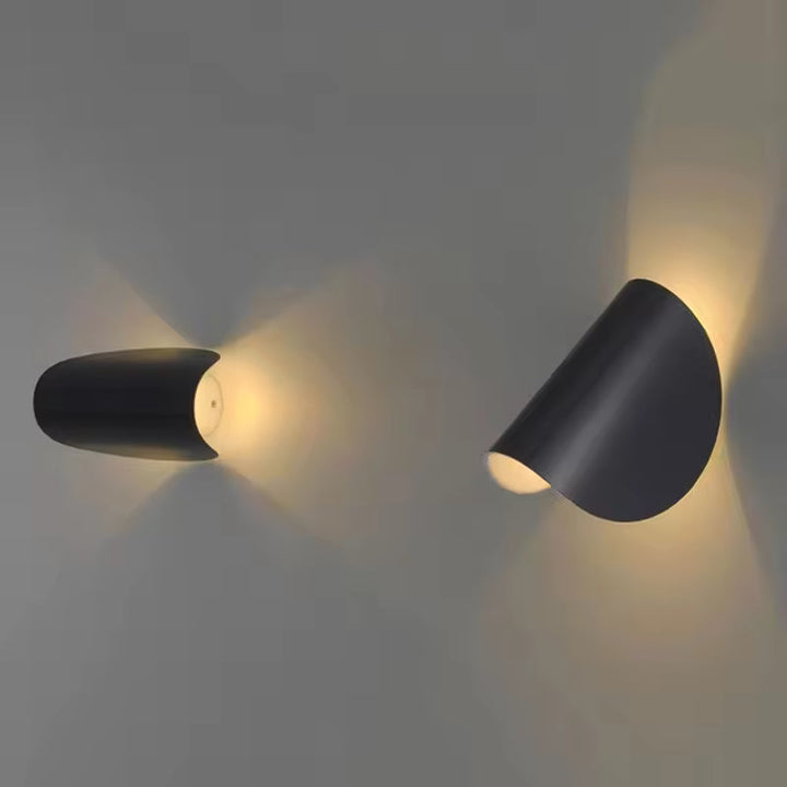 Two black metal wall lights tilted at different angles on a gray wall, with warm light spreading in two directions.
