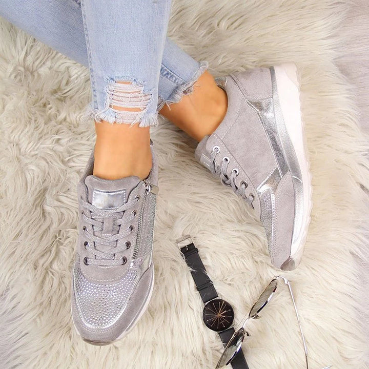 Another view of grey sneakers laid flat on a cream rug next to a black watch and sunglasses.