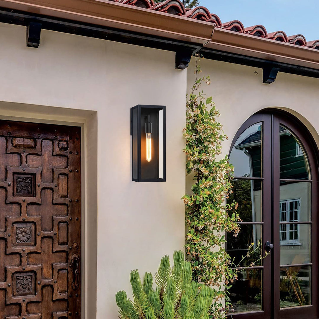 Black outdoor wall lantern with clear glass on a cream stucco wall between a wooden door and an arched window.