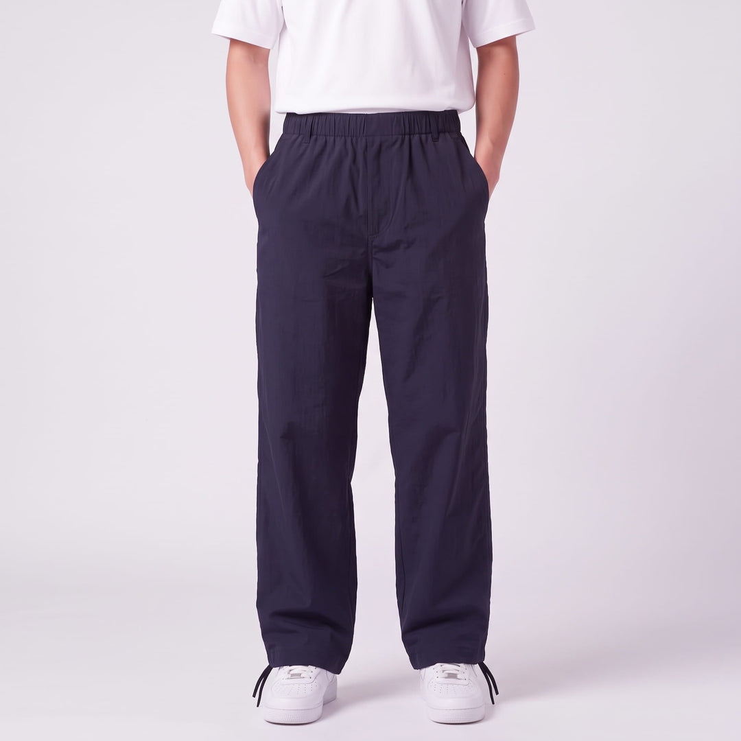 Front view of a model in navy wide-leg pants with elastic waist, hands in pockets, and drawstring cords at the ankles. 1