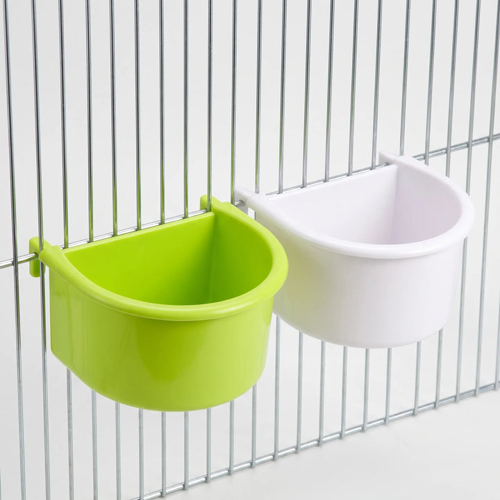 One green and one white half-round bowl hooked onto cage bars, seen at an angle to show the deep, curved inside. 6