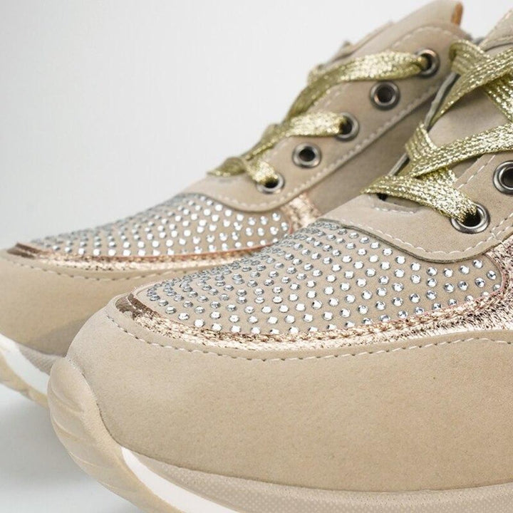 Close-up of the toe area of beige sneakers with gold laces, rhinestone-studded toe panels and rose-gold trim.