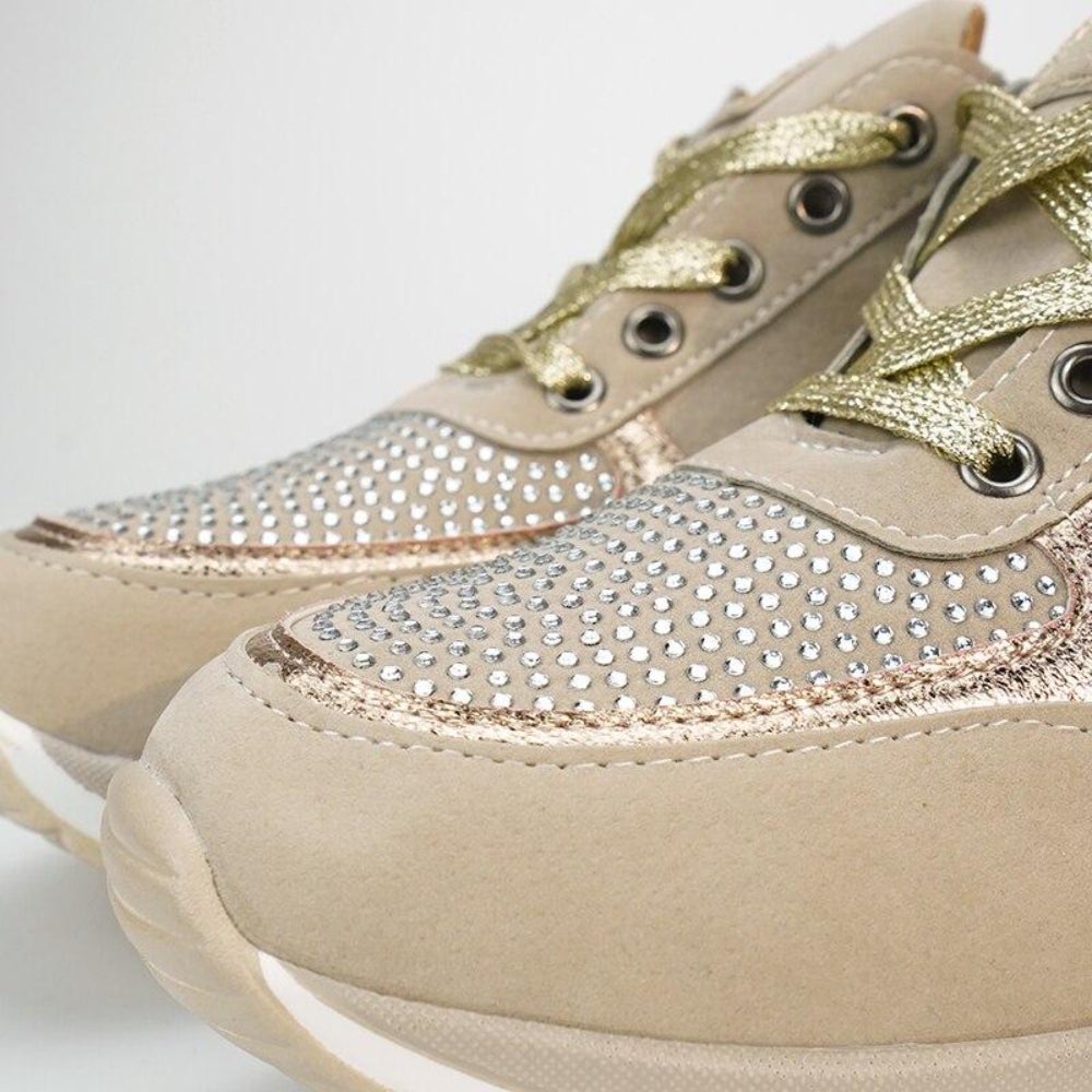 Close-up of the toe area of beige sneakers with a rhinestone-studded vamp, rose-gold trim and gold metallic laces.