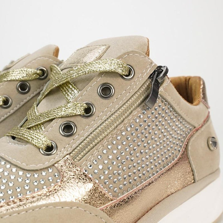 Close-up of a beige sneaker with gold laces, metal eyelets, a side zipper and rows of rhinestones.