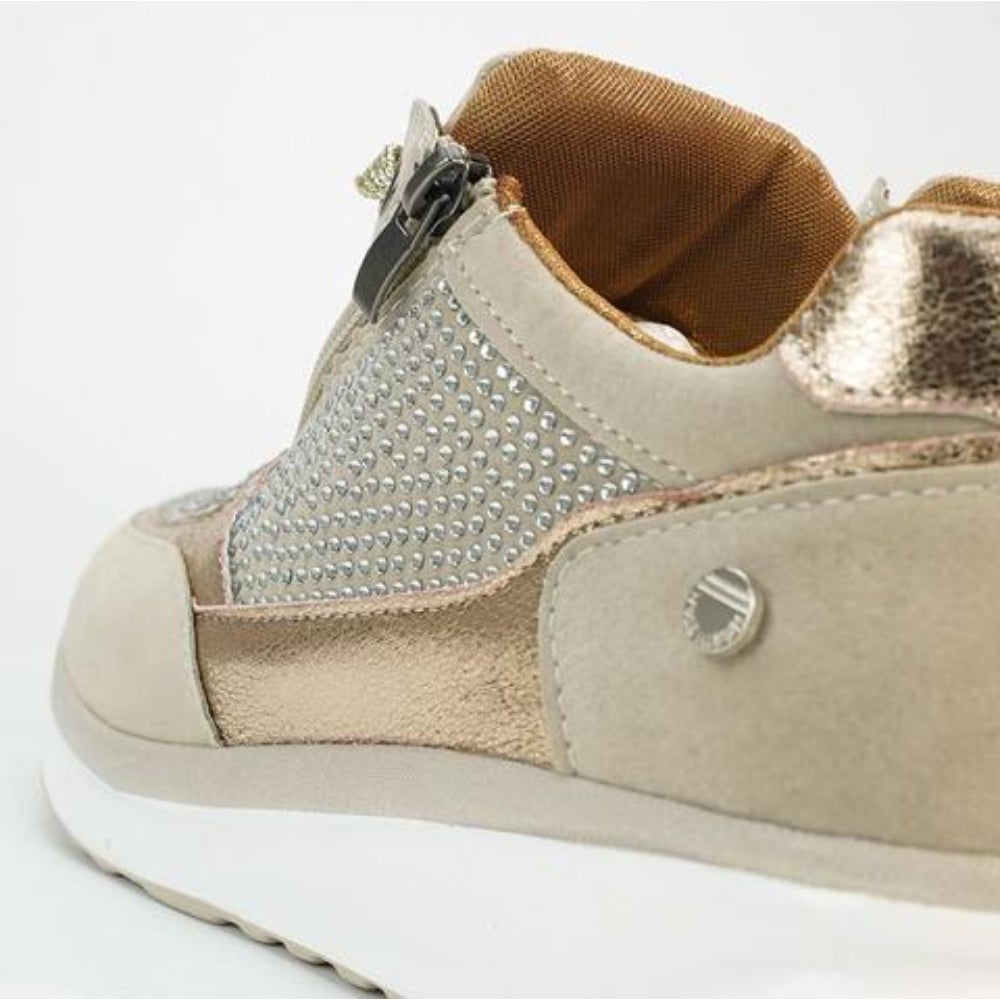 Close-up of the heel and side of a beige sneaker, showing the zipper pull, rhinestone panel, gold lining and metallic heel tab.