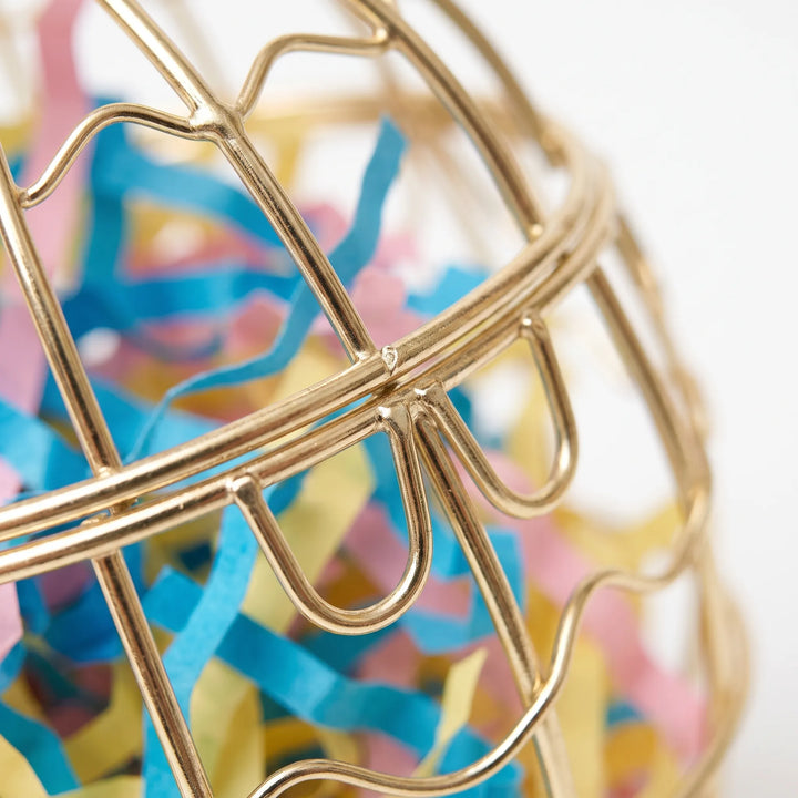 Close-up of the gold wire latch and bars of the cage, filled with shredded blue, pink and yellow paper. 3