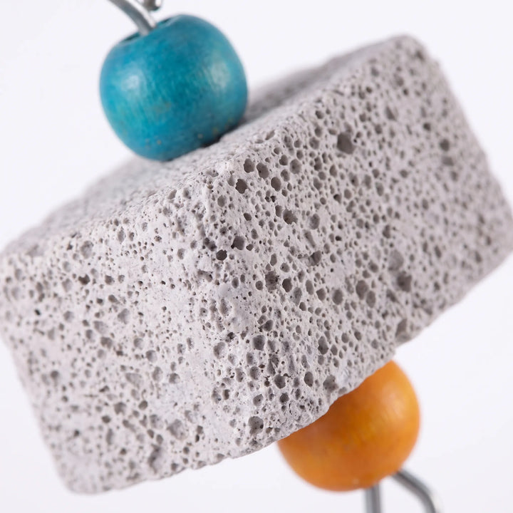Close-up of a porous gray stone block showing its pitted texture, with a blue wooden bead above and an orange bead below. 4