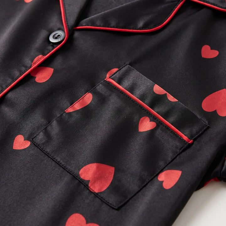 Close-up of the chest pocket, collar and black button on the black satin top, with red piping and red heart print. 5