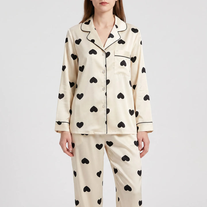 Front view of a model in the long-sleeve cream pajama shirt and pants with black hearts, button front and piped pocket. 6