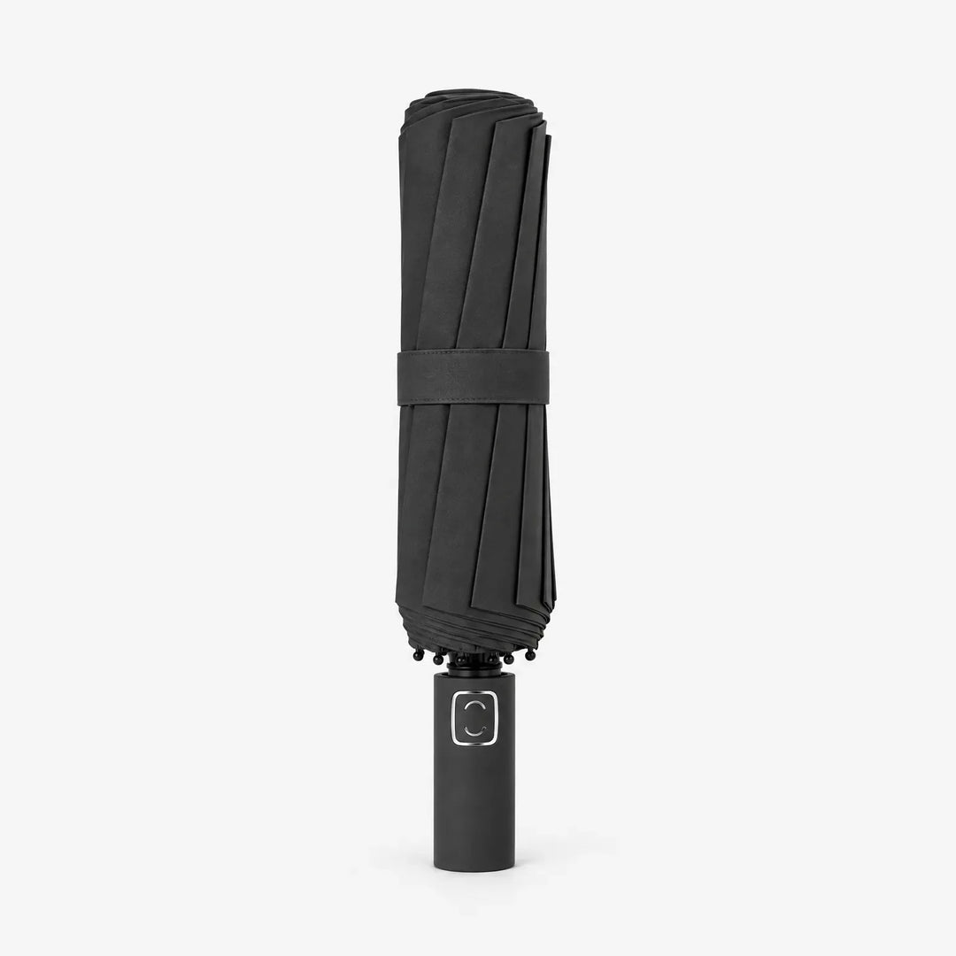 Folded black umbrella standing upright on its handle, wrapped with a matching strap, against a plain white background. 2