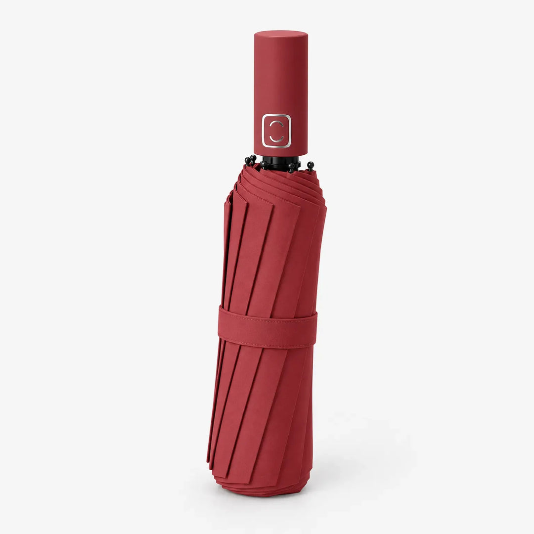 Folded red umbrella with matching strap standing upright, handle on top, shown at an angle on white. 4