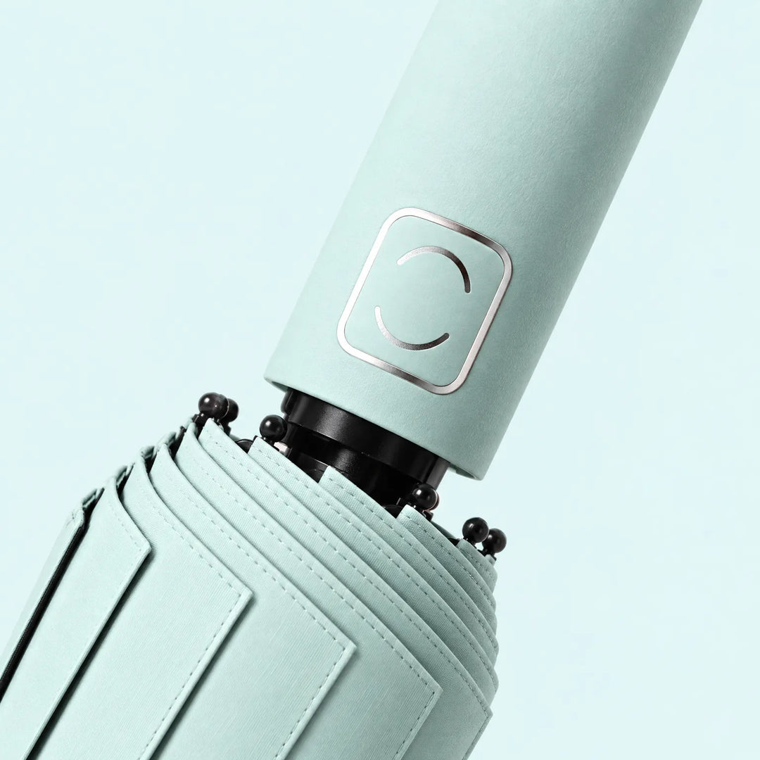 Close-up of a pale mint handle with a metallic square accent and the stitched folded canopy near the black ribs. 5