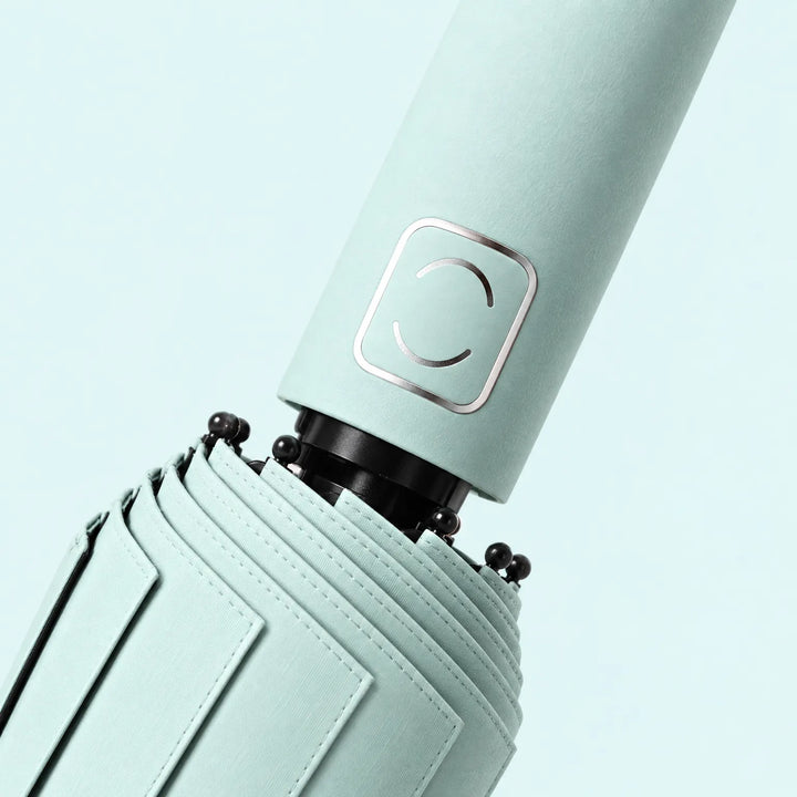 Close-up of a pale mint handle with a metallic square accent and the stitched folded canopy near the black ribs. 5