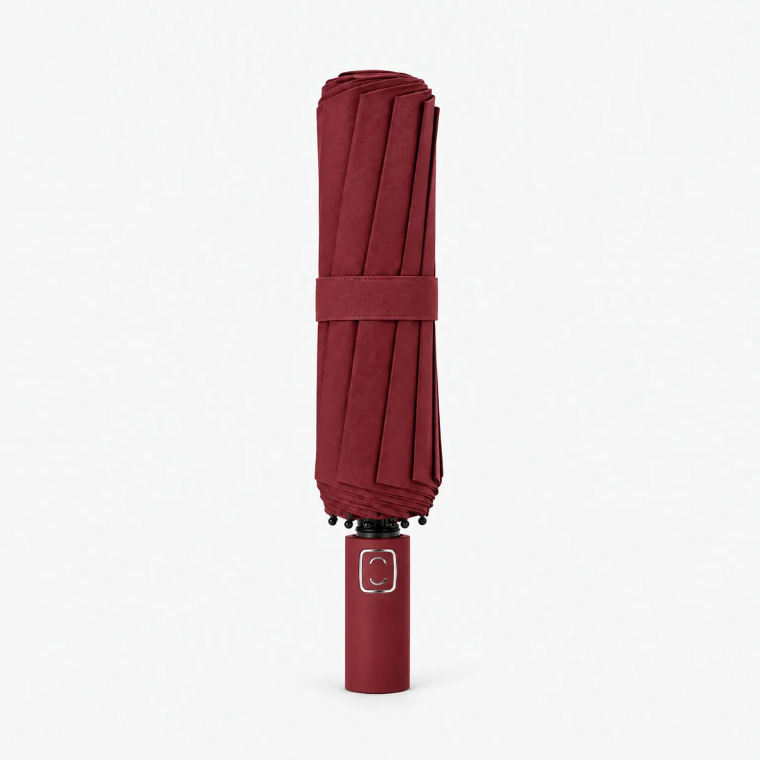 Folded burgundy umbrella with matching strap standing upright on its handle against a white background. 9