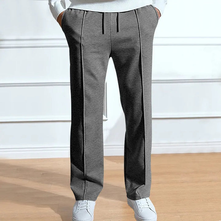 Front view of heather gray drawstring pants with sewn-in creases, worn with white sneakers and a white top, hands in pockets. 2