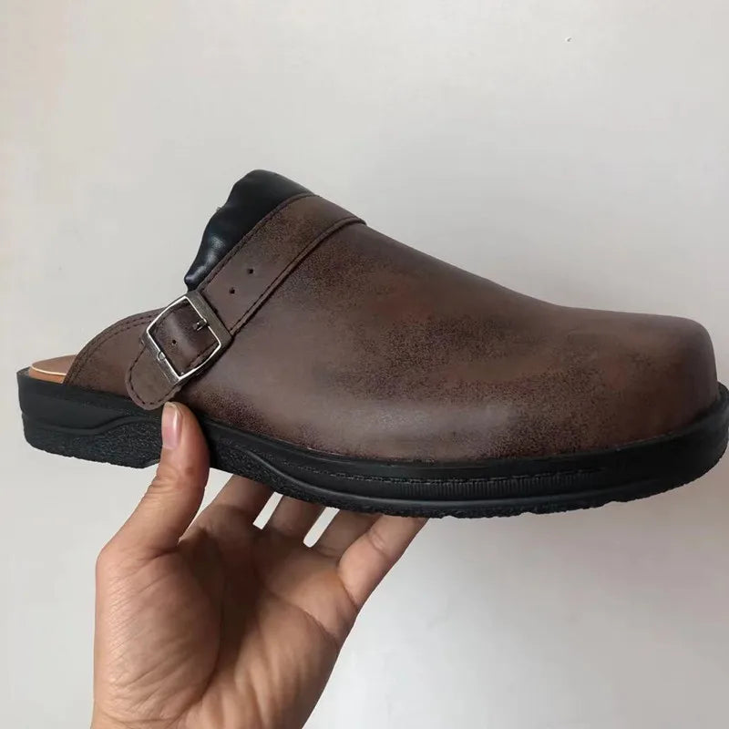 Detail of a single brown clog in side view with a buckle strap, scuffed leather finish and thick black sole.