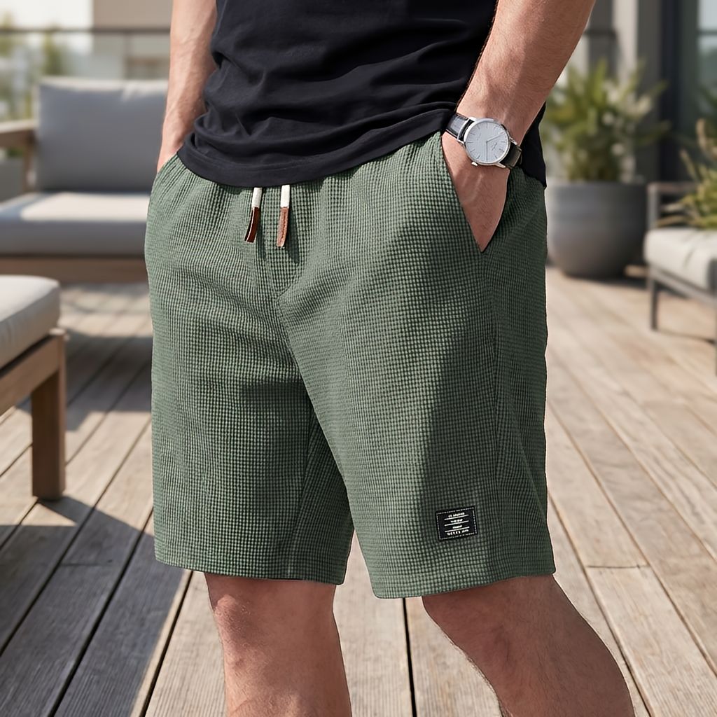 Model wearing olive green waffle-textured shorts with a white and brown drawstring, hand in pocket, on a deck 5