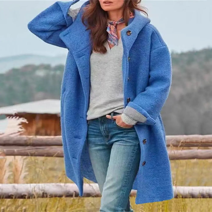 Woman wearing the blue hooded coat open over a gray top, with a scarf, by a fence 5