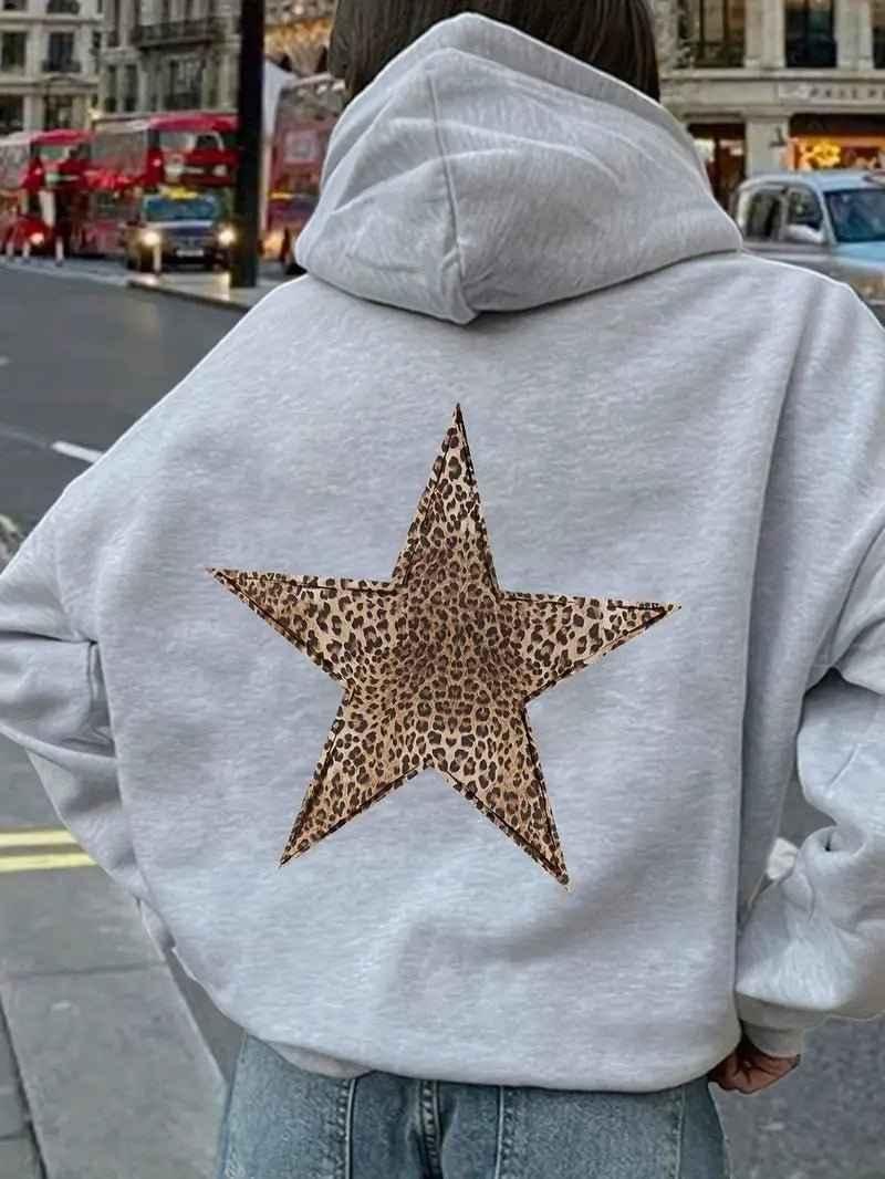 Close back view of a model in a light gray hoodie with the large leopard-print star, standing on a busy city street. 3