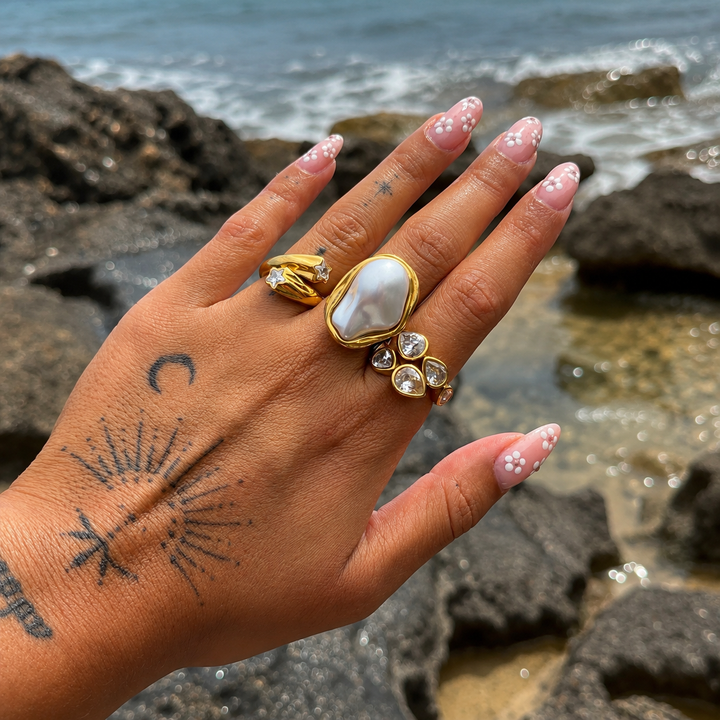 Tattooed hand with floral nails by the sea wearing the gold star ring beside a large pearl ring and crystal ring. 5