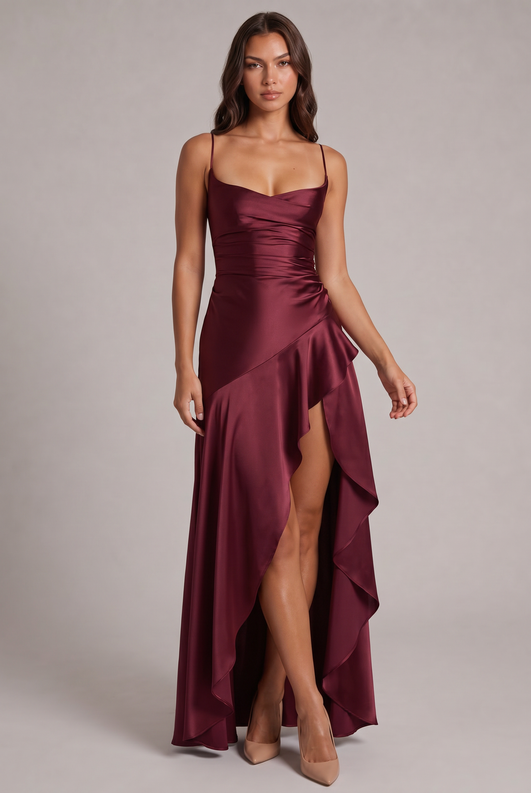 Model wearing the burgundy satin maxi dress, front view, with ruched waist, ruffled slit skirt and nude heels 1