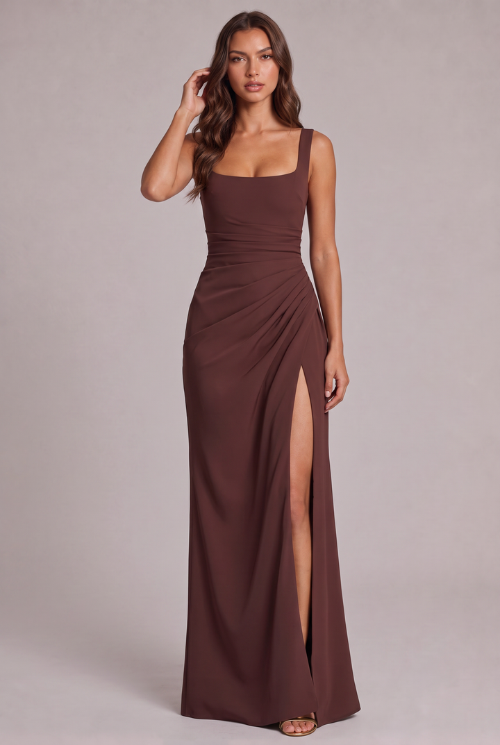 Model in a chocolate brown square-neck maxi dress with ruched waist and high slit, full-length front view, hand touching hair. 5
