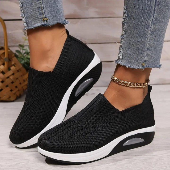 Black knit slip-on sneakers with white platform soles and a clear air cushion window