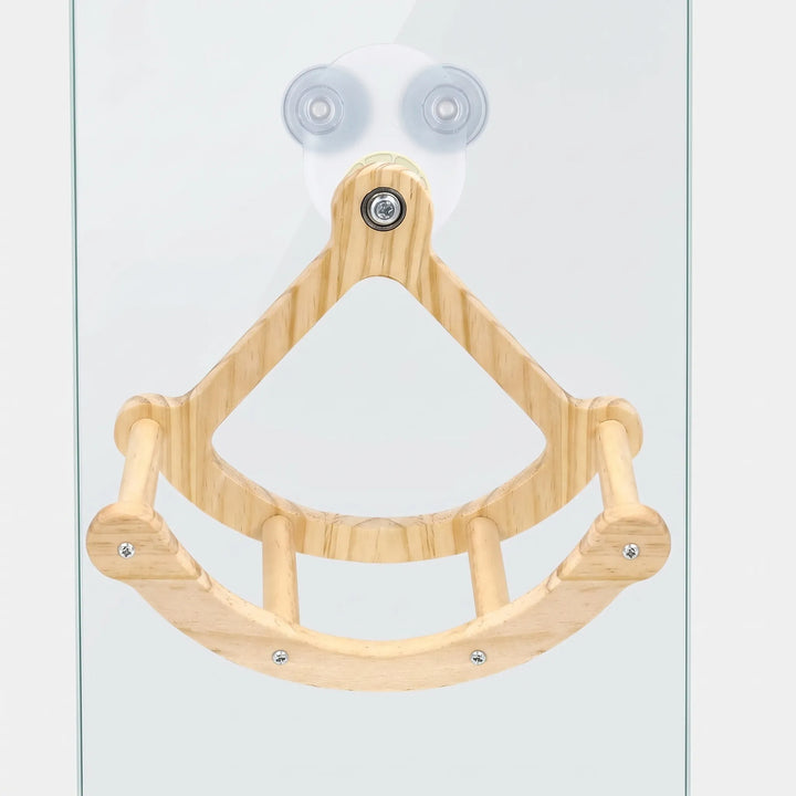 Wooden bird swing with a curved base and dowel perches, mounted on a glass pane by two clear suction cups. 1