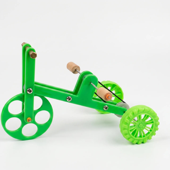 Side view of a small green plastic tricycle toy with wooden foot perches, metal screws and three wheels on a white background. 1