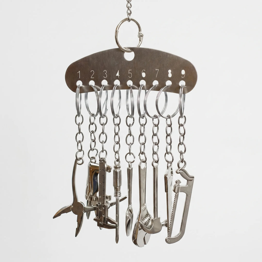 Hanging metal bar with nine numbered holes, each holding a ring and chain that ends in a miniature silver tool charm. 1