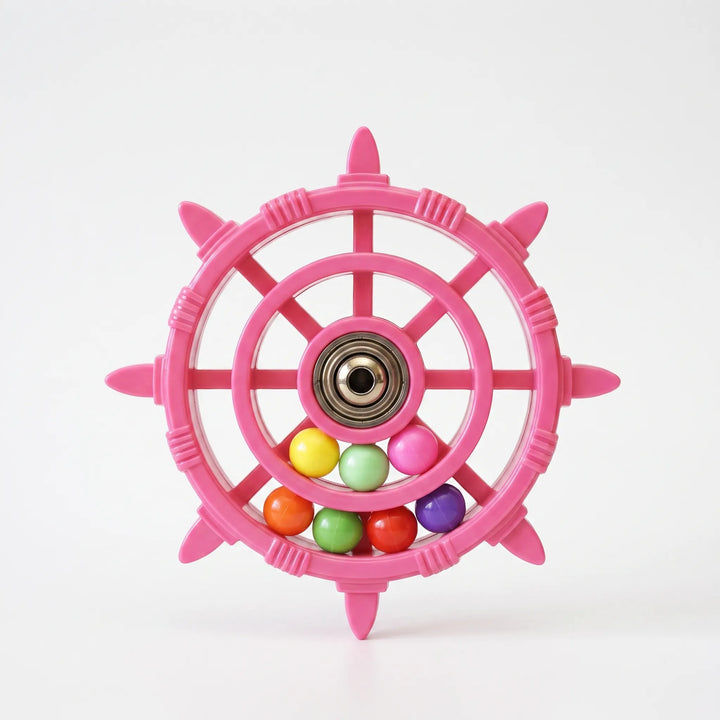 Pink ship-wheel bird toy on a plain white background, showing a metal bearing hub and colorful loose beads inside the rim. 1