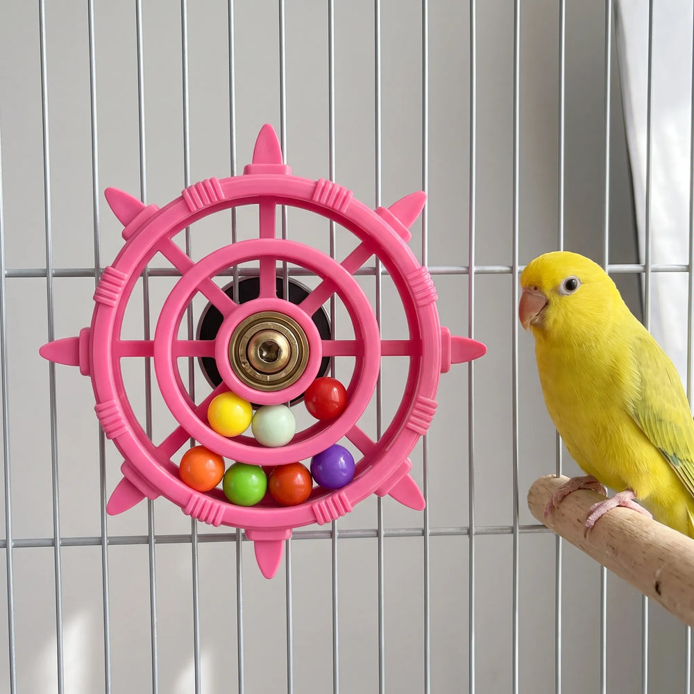 Pink wheel toy mounted on cage bars with a yellow parakeet perched on a wooden branch beside it. 2
