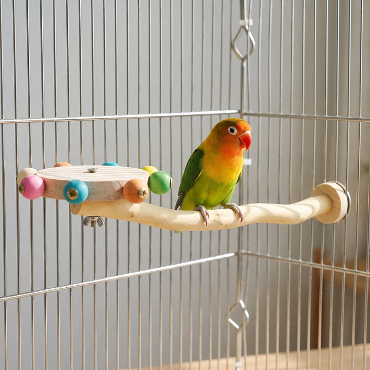 A green, yellow and orange lovebird perched on the wooden branch of the toy, mounted inside a metal cage beside the bead wheel. 2
