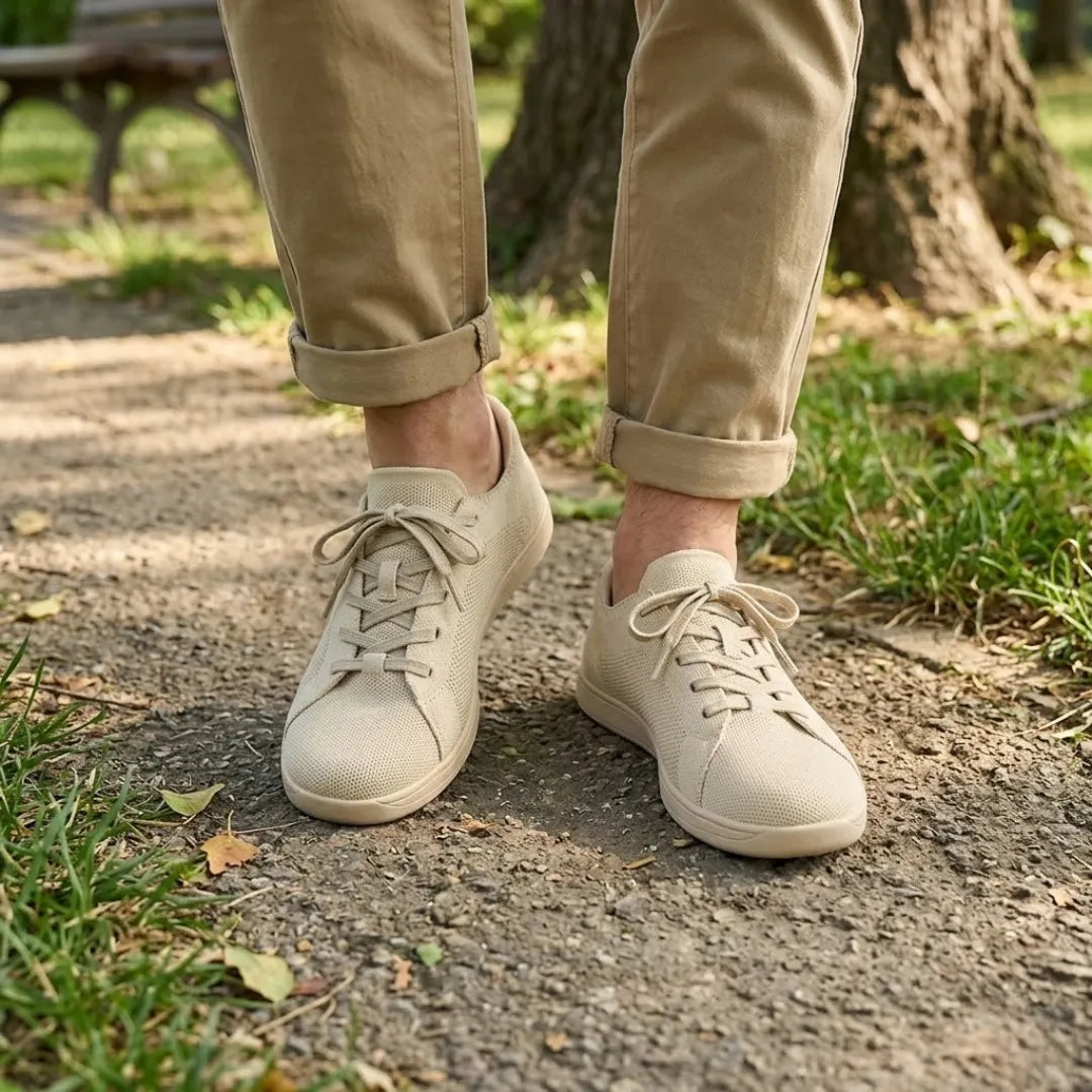 Beige knit sneakers worn with rolled khaki pants on a park path beside grass and fallen leaves.