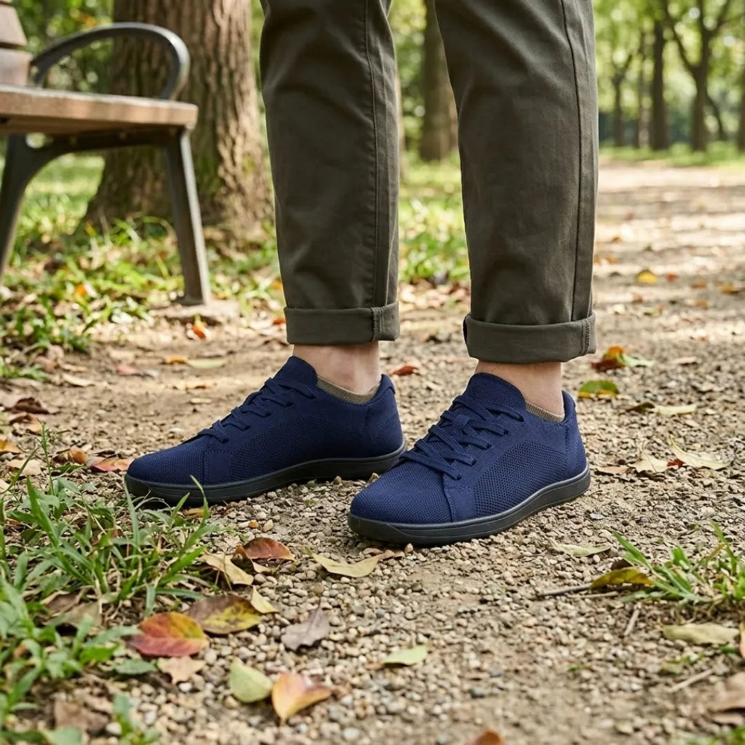 Navy blue knit sneakers with black soles worn with rolled olive pants, standing on a gravel park path near a bench.