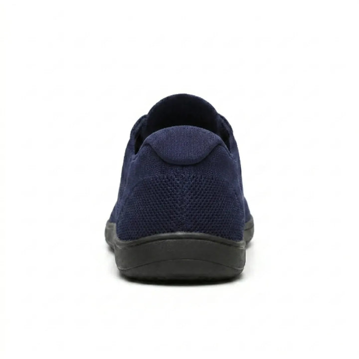 Rear view of a navy blue knit sneaker with black sole, showing the heel tab and textured mesh back. 27