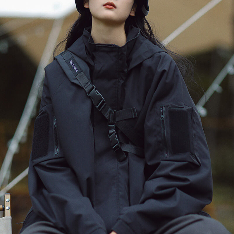 Black hooded jacket with a buckled chest strap and velcro patches on the sleeves.