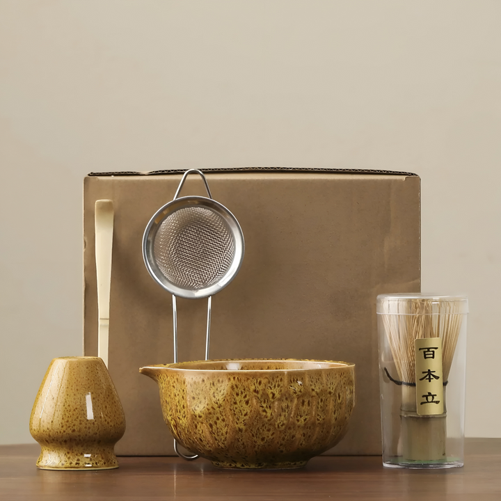 Another view of a mustard-yellow glazed matcha set with whisk holder, sifter, bamboo scoop and whisk in a clear tube.