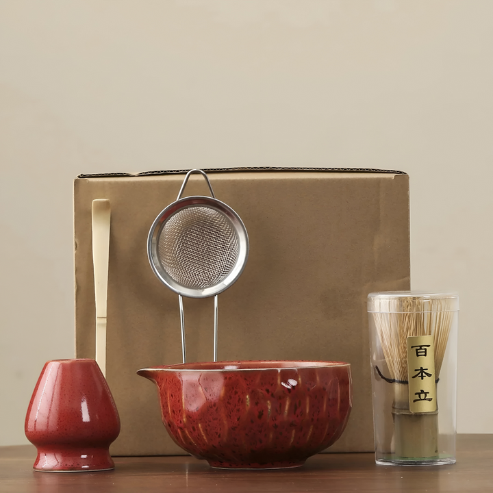 Another view of a glossy deep red matcha set with bowl, whisk holder, sifter, bamboo scoop and whisk in a clear tube.