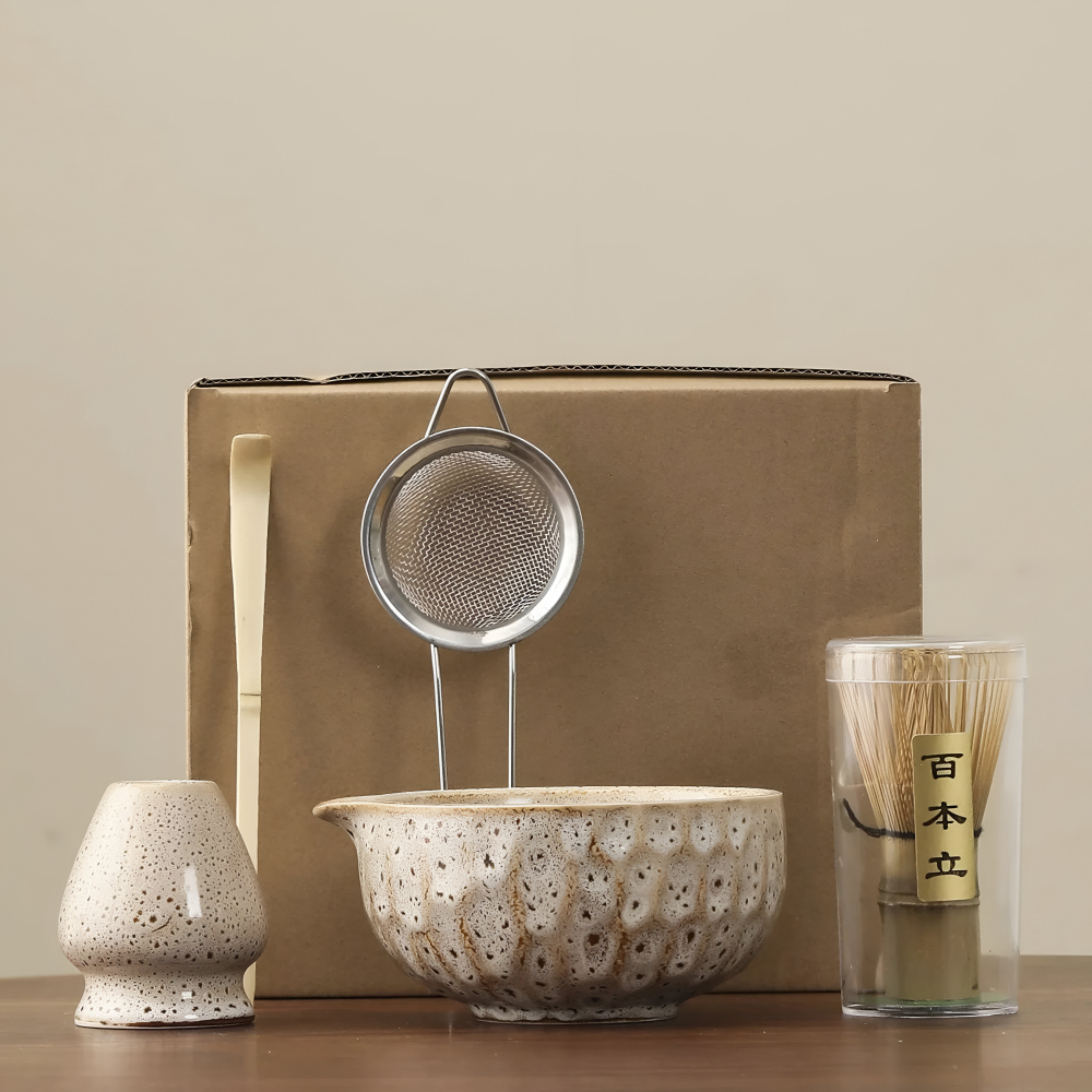 Another view of a cream speckled glazed matcha set with whisk holder, sifter, bamboo scoop and whisk in a clear tube.