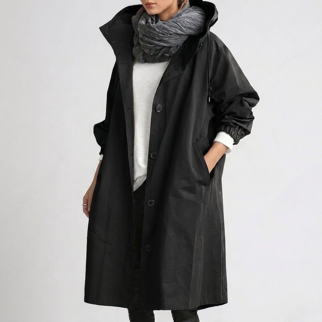 Women's Raincoat in black with hood and button front, shown with a hand in the pocket.